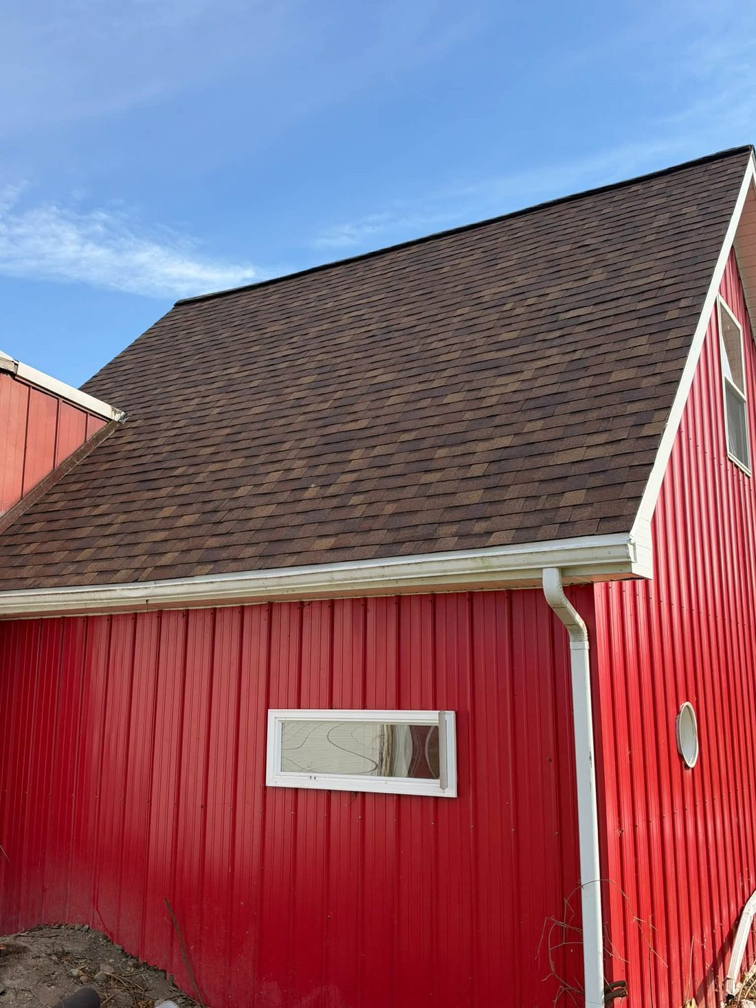 A new shingle roof and gutters on a red barn by Royalty Exteriors